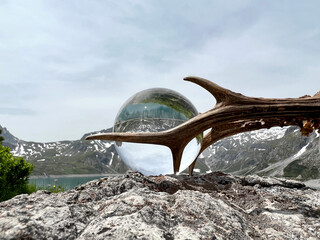 Roebuck antlers next to Lensball, crystal ball, with reflections of Lake Lunersee (Lünersee, Montafon, Vorarlberg). In the background the famous high mountains of austria and switzerland (Rätikon).
