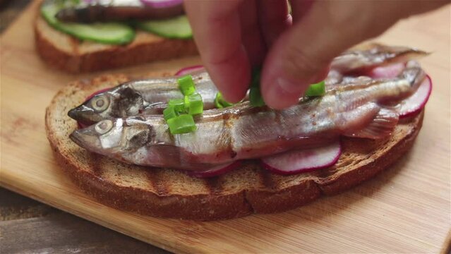 man hand put chopped chives on sandwich with salted capelin sardines radish rye bread close up