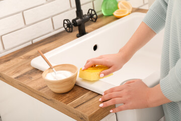 Woman cleaning white sink with sponge and baking soda