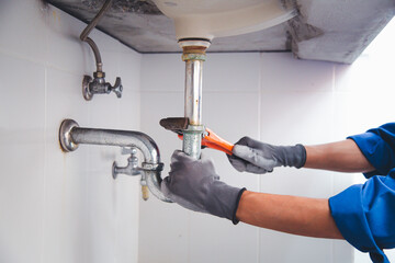 Technician plumber using a wrench to repair a water pipe under the sink. Concept of maintenance, fix water plumbing leaks, replace the kitchen sink drain, cleaning clogged pipes is dirty or rusty. - obrazy, fototapety, plakaty