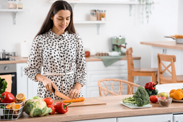 Young woman cutting carrot in kitchen
