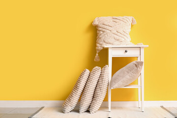 Table with stylish pillows near yellow wall in room