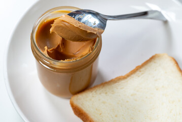 A bottle of creamy peanut butter by the plain loaf bread 