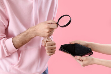 Young man with magnifier looking at empty wallet on pink background, closeup