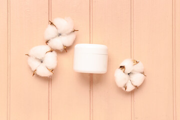 Jar of cosmetic product and cotton flowers on color wooden background