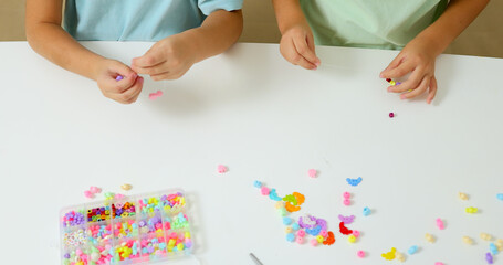 Little girls putting beads together in bracelet. Child's handicraft concept. 