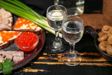 Shots with cold vodka and snacks on dark wooden background