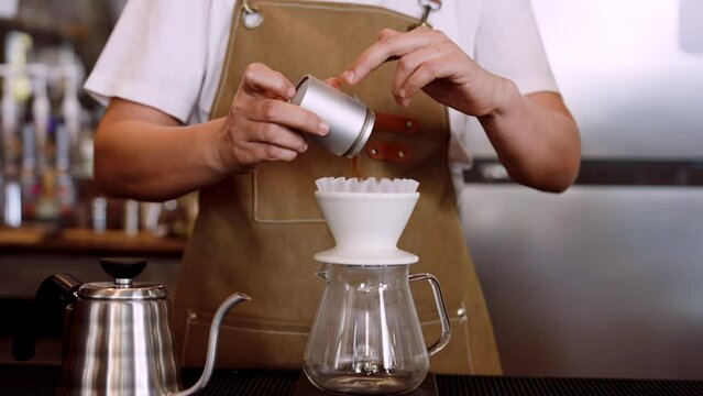 Close-up machine that supports coffee powder from grinder, with coffee powder inside, barista is pouring coffee powder into glass jug that, make coffee powder into fresh coffee drink.