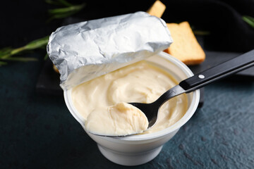 Plastic container with tasty cream cheese on black background