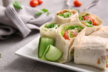 Plate of tasty lavash rolls with vegetables on grey background