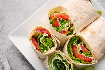 Plate of tasty lavash rolls with vegetables on grey background