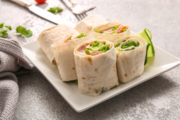 Plate of tasty lavash rolls with vegetables on grey background