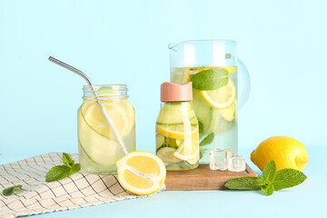 Sports bottle and jug of lemonade with cucumber on blue background