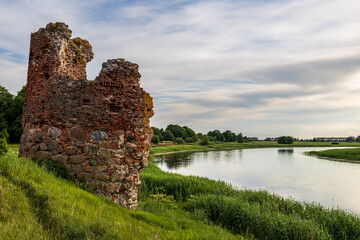 an old crumbling tower by the river in summer and there is a blue cloudy sky - obrazy, fototapety, plakaty