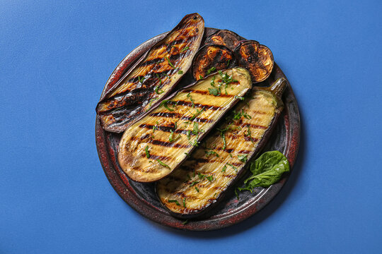 Plate with delicious grilled eggplants on blue background