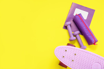 Skateboard with dumbbells, pencil case and notebook on yellow background