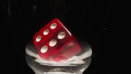 Red gaming cube with white dots floating in transparent wineglass at studio light on black background. Dice for gambling casino games with six points on each face macro - Powered by Adobe