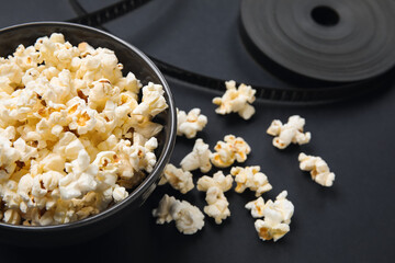Bowl with tasty popcorn and film reel on black background