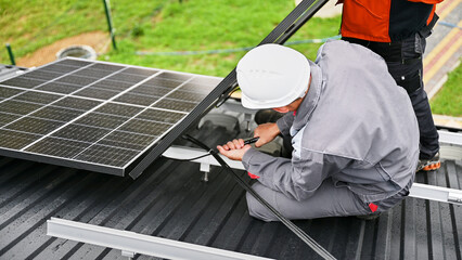 Mounters connecting cables while installing photovoltaic solar panels on roof of house. Workers...
