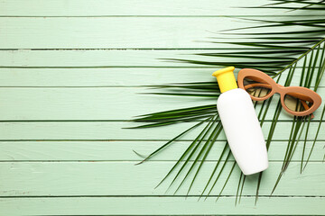 Sunglasses with bottle of sunscreen cream and palm leaf on green wooden background