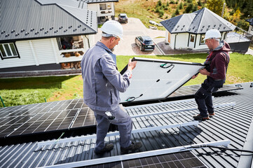Mounters building solar panel system on roof of house. Men workers in helmets carrying photovoltaic...