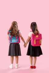 Little schoolgirls holding hands on pink background, back view