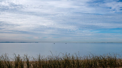 Beach at Scarborough, Queensland, Australia on a cloudy day with calm water on Moreton Bay. Moreton Island can be seen in the distance along with some small boats with people fishing.