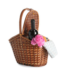 Wicker basket with tasty food for picnic, wine and peony flower on white background