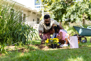African american father planting flowers with daughter and son on field in backyard