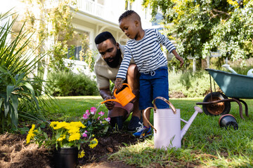 African american father with son watering flower pots and plants in yard