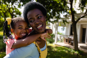 Close-up of african american cheerful mother piggybacking daughter while standing in backyard