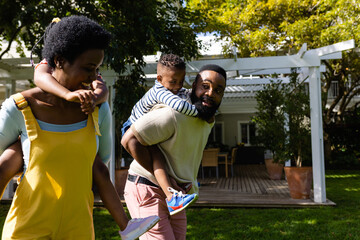African american parents piggybacking son and daughter while walking in backyard on sunny day