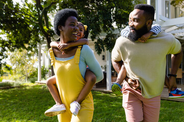 African american cheerful parents piggybacking children while walking in backyard