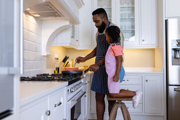 African american daughter looking at father cooking pancakes on stove in kitchen