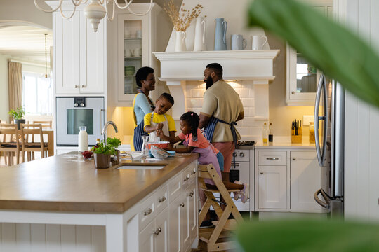 African american siblings mixing batter in bowl on kitchen island with parents in background at home - Powered by Adobe