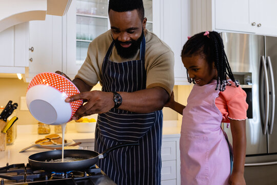 Happy african american father with daughter cooking pancakes in pan in kitchen