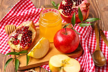 Board with jar of honey, ripe pomegranates and apple on wooden table, closeup. Rosh hashanah (Jewish New Year) celebration
