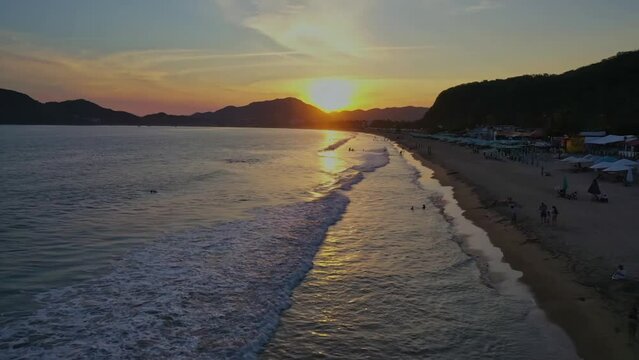 Vuelo de dorne sobre una playa turistica mientras cae el atardecer en playas de Colima, M&eacute;xico.