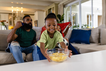 Happy african american parents with son and daughter with flag watching sport on tv at home