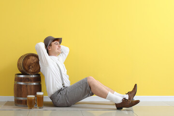 Young man in traditional German clothes with beer sitting near yellow wall