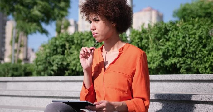 Happy young African American woman using digital tablet pad sufring internet inspired with new ideas sitting outdoors
