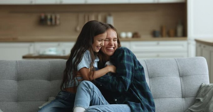 Joyful mother and daughter fool around on couch, play active games, laughing, screaming, having fun, young mom tickling excited kid feel overjoyed, show care and love, enjoy warm family relationship