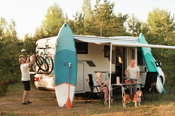 A happy family is resting nearby near their motorhome in the forest
