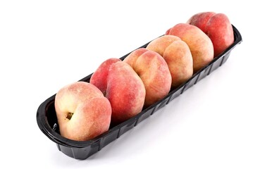 Flat peaches, known also as doughnut peaches, in a row on a narrow black plastic tray. White...