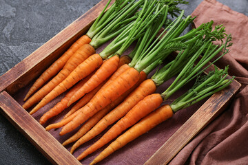 Tasty fresh carrots and wooden board on black textured background