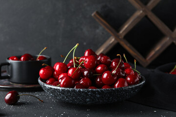 Bowl and cup with sweet cherries on black background