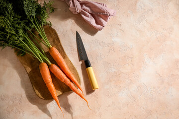 Wooden board of fresh carrots with leaves on beige background