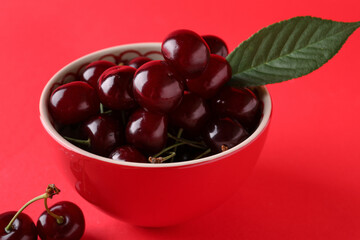 Bowl with sweet cherries and leaf on red background