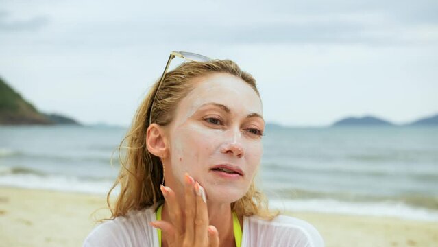 Portrait woman applying sun cream protection lotion.Woman looking at camera on beach near sea smearing sunscreen cream on face.Concept facial beauty skin care, hygiene treatment, moisturizer cosmetic