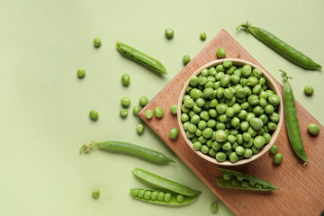 Bowl and wooden board with fresh green peas on color background